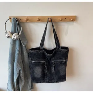 Detailed view of dark grey washed denim tote bag featuring dual zippers and tassel details