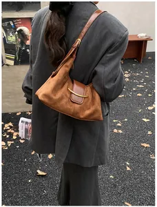 Sac hobo vintage en daim marron avec détails dorés porté à l'épaule en extérieur