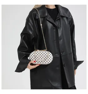 Polka dot hard shell evening clutch with gold chain strap shown on black leather coat