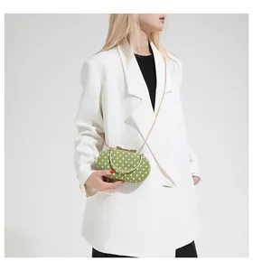 Detail of green polka dot handbag with gold chain strap and metal handle on a model
