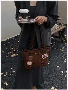 Détail du sac cabas marron foncé avec écussons de dessins animés et lanières en cuir de qualité