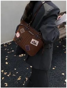 Détail d'un sac cabas marron vintage avec écussons brodés et bandoulière en cuir