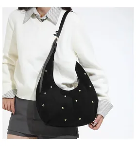 Détail d'un sac hobo en daim noir avec clous dorés et bandoulière réglable sur modèle