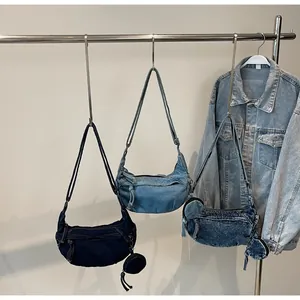 Drei Nuancen von Denim-Halbmond-Umhängetaschen mit Quasten auf einem Metallständer