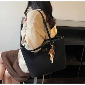 Detail of a large black tote bag with matte texture and decorative ethnic wood bead charm