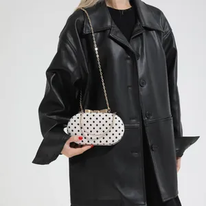 Polka dot white oval crossbody chain bag with gold metal handle on model in leather jacket