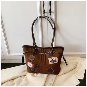 Détail du sac cabas marron vintage avec écussons brodés et logo métallique chic