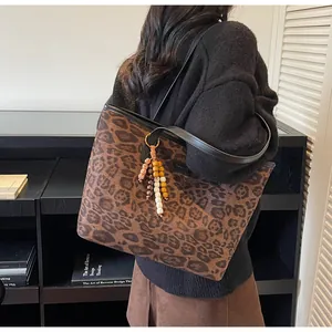 Close-up of a leopard print tote bag with colorful wooden bead charm and long shoulder strap