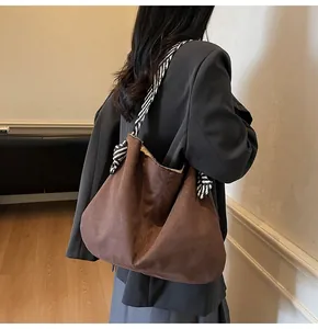 Detail of brown suede tote bag with black and white striped woven strap and bow accent