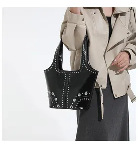 Detail of studded black patent leather tote bag styled with a beige biker jacket