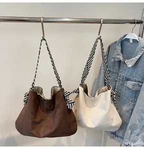 Detail of suede shoulder bags in brown and beige with woven handles and side bow accents