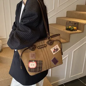 Grand sac cabas en cuir marron avec écussons et longues anses, porté par un mannequin