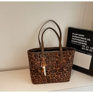 Detail of leopard print tote bag featuring wooden beaded tassel and smooth brown handles