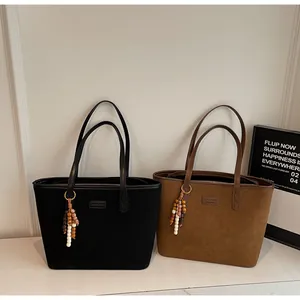 Close-up of matte suede tote bags in black and brown with ethnic tassel charms