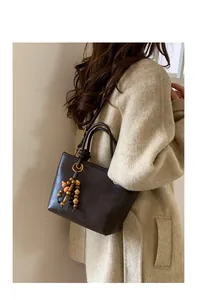Detail of dark brown tote bag with beaded charm on a beige tweed coat outfit