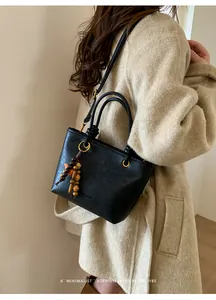 Detail of black leather bucket bag with matte texture and decorative wooden beads