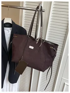 Detail einer dunkelbraunen Wildleder-Tragetasche mit Modelabel und kariertem Bandakzent