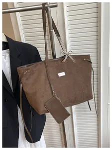 Detail der braunen Wildleder-Tragetasche mit Metalletikett und kariertem Schleifenanhänger