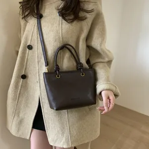 Dark brown faux leather bucket bag with knot handles and long strap in street style