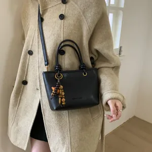 Elegant black leather bucket bag with wooden beads tassel worn with a beige coat