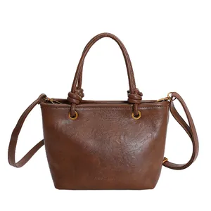 Brown faux leather bucket bag with top handles, gold hardware, and shoulder strap