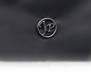 Macro view of silver JP logo emblem on black minimalist leather shoulder bag
