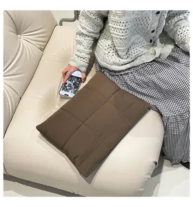 Detailed texture of dark brown quilted puffer laptop sleeve on a soft leather sofa