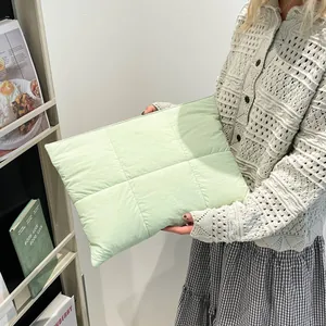 Minimalist light green quilted laptop sleeve held by a model in a bright, modern setting