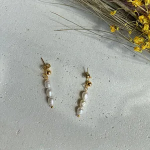 Dettaglio macro di eleganti orecchini pendenti in oro con tre perle d'acqua dolce