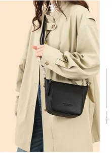 Close-up of black lychee grain leather crossbody bag shown on model with beige coat