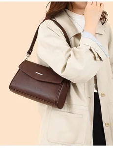 Detail of elegant dark brown leather handbag featuring a sleek silver metal bar on the flap