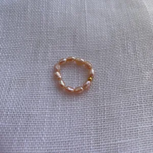 Makroaufnahme eines Süßwasser-Barockperlenrings mit Goldperle auf weißem Stoff