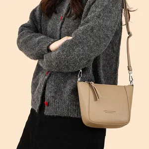 Khaki pebbled leather bucket bag with tassels and adjustable strap on a female model