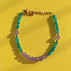 Close-up of handmade beaded bracelet with green and purple stones and gold lobster clasp