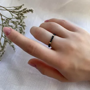 Detail of handcrafted beaded ring with black faceted stones and gold accents on finger