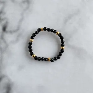 Detail of beaded ring with faceted black stones and golden accents on marble surface