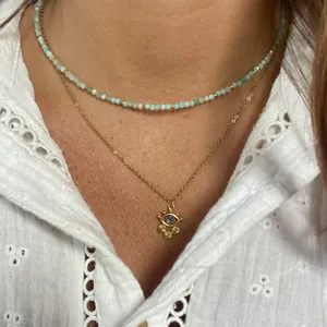 Detail of layered gold necklace with mint beads and evil eye pendant with charms