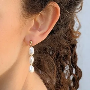 Primo piano di orecchini a tre perle d'acqua dolce barocche con perno dorato su modella