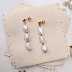 Dettaglio di orecchini pendenti con perle barocche dorate su custodia in camoscio beige