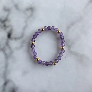 Macro detail of elastic bead ring with faceted purple stones and polished gold beads