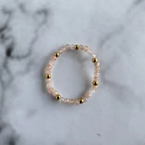Macro detail of elastic bead ring with faceted peach gemstones and polished gold beads