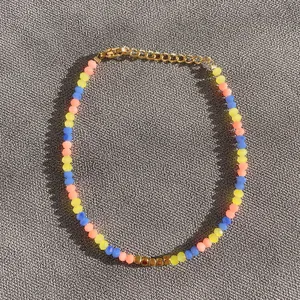 Détail d'un bracelet en perles colorées avec carrés dorés et fermoir mousqueton