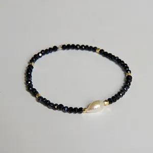 Gros plan d'un bracelet de perles noires à facettes avec une perle goutte blanche et dorure