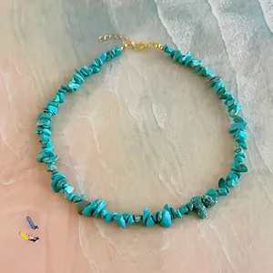 Détail du collier en éclats de turquoise avec fermoir mousqueton doré sur fond de plage