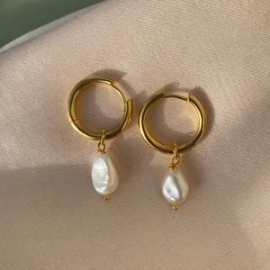 Gros plan sur des boucles d'oreilles créoles dorées et perles baroques sur soie