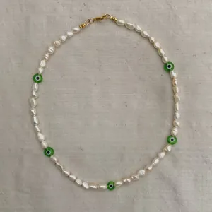 Detail of baroque pearl necklace featuring green evil eye beads and golden lobster clasp