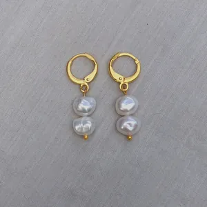 Détail macro de boucles d'oreilles créoles dorées avec perles baroques sur tissu gris