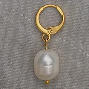 Élégante boucle d'oreille dorée avec perle baroque blanche sur tissu gris texturé