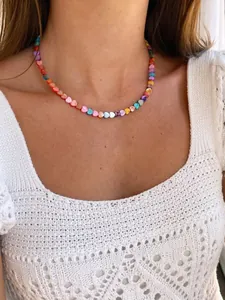 Detailed view of colorful heart-shaped beaded necklace on model in white crochet top