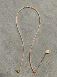 Detail of colorful beaded necklace featuring a golden heart pendant and lobster clasp
